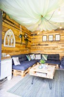 Inside a small summerhouse with wooden walls, pallet sofas and a pallet coffee table on a rug