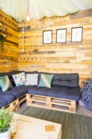 Inside a small summerhouse with wooden walls, pallet sofas and a pallet coffee table on a rug