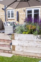 Parasol over garden table and chairs on patio behind raised beds planted with Artemisia 'Powis Castle', Euphorbia characias 'Silver Swan'
and Salvia nemorosa 'Caradonna'