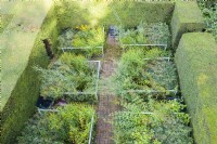 View over garden enclosed by hedges of clipped Yew, planted with later flowering perennials and with six beds separated by brick paths and contained by railings. September. Image taken with drone.