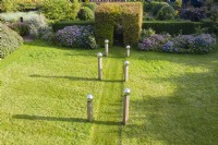 Meadow that has been cut with avenue of columns of wood capped with stainless steel globes and backed by border of Hydrangeas and a clipped tunnel of Hornbeam. September. Image taken with drone. 