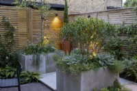 Courtyard garden at dusk with stone raised beds and contemporary wood boundary fence and lighting