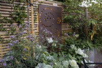 Courtyard garden at dusk with raised beds and contemporary wood boundary fence with metal screen and lighting