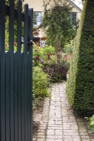 A gate opens onto a brick path leading into a country garden in August.