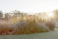 Frosted rustic coppiced ash gazebo and backlit grasses and perennials at sunrise.