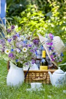 Set for picnic with wildflower bouquet in a jug and a hat with a wreath.