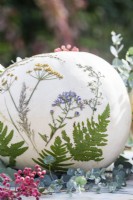 White pumpkins with pressed flowers and leaves on table with berries and eucalyptus sprigs