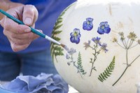 Woman painting glue over pressed flowers to stick them to the pumpkin