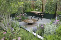 Woven willow panels with Trachelospermum jasminoides - star jasmine - and metal raised planter screens enclose a striking weathered mild steel water feature with wildlife-friendly plants including Hyssopus, Calamintha, Salvia, Echinacea purpurea 'Magnus' and Rosa 'Princess Alexandra of Kent'.  The Landform Mental Wealth Garden - RHS Hampton Court Palace Garden Festival 2023.  Gold medal winner.  