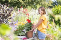 Woman planting Dahlia in terracotta pot at potting bench