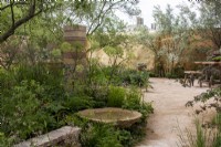 View through The Nurture Landscapes Garden  with a circular water feature, wall and column made from waste materials- designer Sarah Price - RHS Chelsea Flower Show 2023