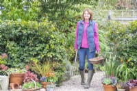 Woman walking along stone path carrying a digging fork and a trug full of tulip bulbs