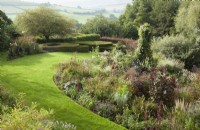 View over lawn and borders to contemporary box and yew topiary with country views beyond.