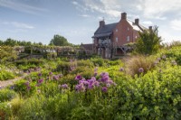 View over the gravel garden towards the farmhouse with Alliums and mixed planting flower beds with ornamental grasses
