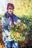 Woman holding up wreath made up of Beech sprigs, Portuguese laurel sprigs, Teasel heads and Hawthorn twigs