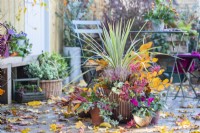 Container planted with Phormium 'Tenax', Callunas, Ivy, Beech sprigs and Rowan - Sorbus berries with smaller pots planted with Ivy and Cyclamen with leaves scattered across the deck