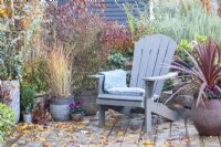 Recycled plastic chair with cushion and blanket surrounded by mixed planting and leaves scattered across a wooden deck