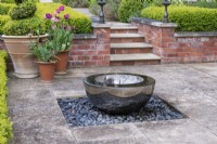 A stainless steel, black water bowl from David Harber, sits on a bed of grey pebbles.
