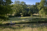 Large natural wildlife pond, edged with wildflowers and grasses, small landing stage with wooden rustic seats