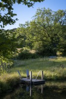 Large natural wildlife pond, edged with wildflowers and grasses, small landing stage with wooden rustic seats