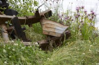 Twisted rusty metal machinery in wildlife garden with Monarda flowers. Summer.
