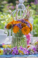 Bunch of summer flowers including pot marigold, verbena, persicaria and coneflowers in a small glass vase.