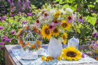 Wreath made of summer flowers hanging from bird cage and bouquet in enamel jug containing sunflowers, coneflowers, wild carrots and fennel.