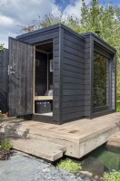 Timber wooden deck over a pool - black painted wood sauna cabin with a living roof planted with wildflowers and herbs