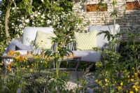 Patio seating area with table and chairs with cushions and a drystone wall with corten steel bird boxes, Viburnum opulus against the wall