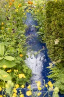 A modern contemporary water rill made from recycled plastics with mixed perennial planting of Geranium phaeum 'Raven', Trollius chinensis 'Golden Queen', Ranunculus acris and a Taxus baccata - Yew hedge