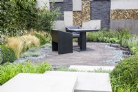 Stone steps leading to a brick paved patio area with black table and chairs, wall made from grey brick and concrete slabs