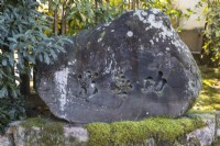 Stone with inscription in Japanese sitting on moss covered stone surface. 