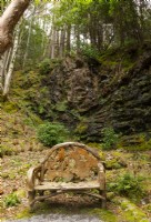 A rustic style carved wooden chair beside a rocky cliff in the Rhododendron dell.