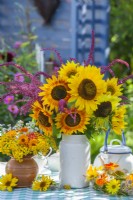 Summer wreath and bouquets with sunflowers, amaranthus, nasturtium, pot marigolds and tansy in vases on the table.