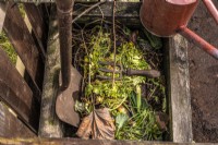 Small wooden compost bin with dead leaves, peelings, compost material and vintage garden tools