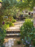 Path and steps made of bricks and gravel leading to dining area. The Nurture Landscapes Garden, Designer: Sarah Price, Gold medal winner Chelsea Flower Show 2023