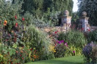 Tropical-style planting sits either side of a wrought iron gate in an old brick wall at The Manor, Little Compton.