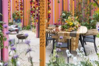 View of the dining area with table and chairs decorated with Indian style ornaments, colourful flowers, fruits and spices. Orange post with sentences in braille on the front. The RHS and Eastern Eye Garden of Unity, Designer: Manoj Malde