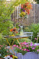 Container plantings on the terrace with Impatiens and Pelargonium, a flower arrangement with a cold drink on the table.