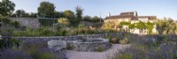 Small circular pond with stone sides in drought tolerant garden planted with Lavender, Verbena hastata and Heleniums.  The Walled Garden at Staverton, Devon