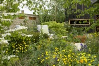 RHS Chelsea Flower Show 2023 - The RSPCA Garden designed by Martyn Wilson Silver Gilt, in foreground viburnum plicatum Watanabe with buttercups beyond a seating area 
