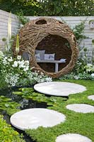 Willow arbor in a small garden with pond and chamomile as a lawn substitute 