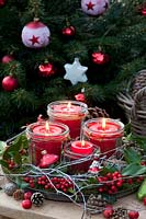 Advent wreath with candles in jars on a tray, decorated with moss, holly branches and cones 
