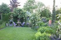 Country house garden with seating area under pear tree, perennials and roses 