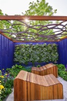 Relaxation area surrounded by a navy blue painted panels with decorative wooden deckchairs set against living green wall under with geometric design openwork of pergola roof.  June
Bord Bia Bloom, Dublin
Designer: Jane McCorkell



