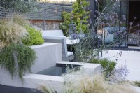 Water feature surrounded with the planting of Rosmarinus officinalis 'Prostratus Group', Stipa tenuissima, Pittosporum tobira 'Nanum' and Verbena bonariensis.