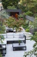 Overview of this city garden with the sitting area with multistem Parrotia persica, sun lounger and path leading to the zinc clad bulding 