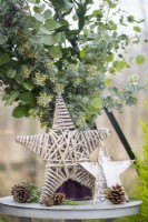 Wicker and birch stars on table with pinecones and a jug of sprigs