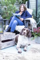 Dog laying by woman on chair with magazine in inside decorated greenhouse