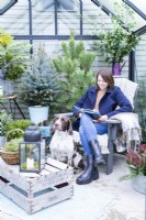 Dog sitting by woman on chair with magazine in inside decorated greenhouse